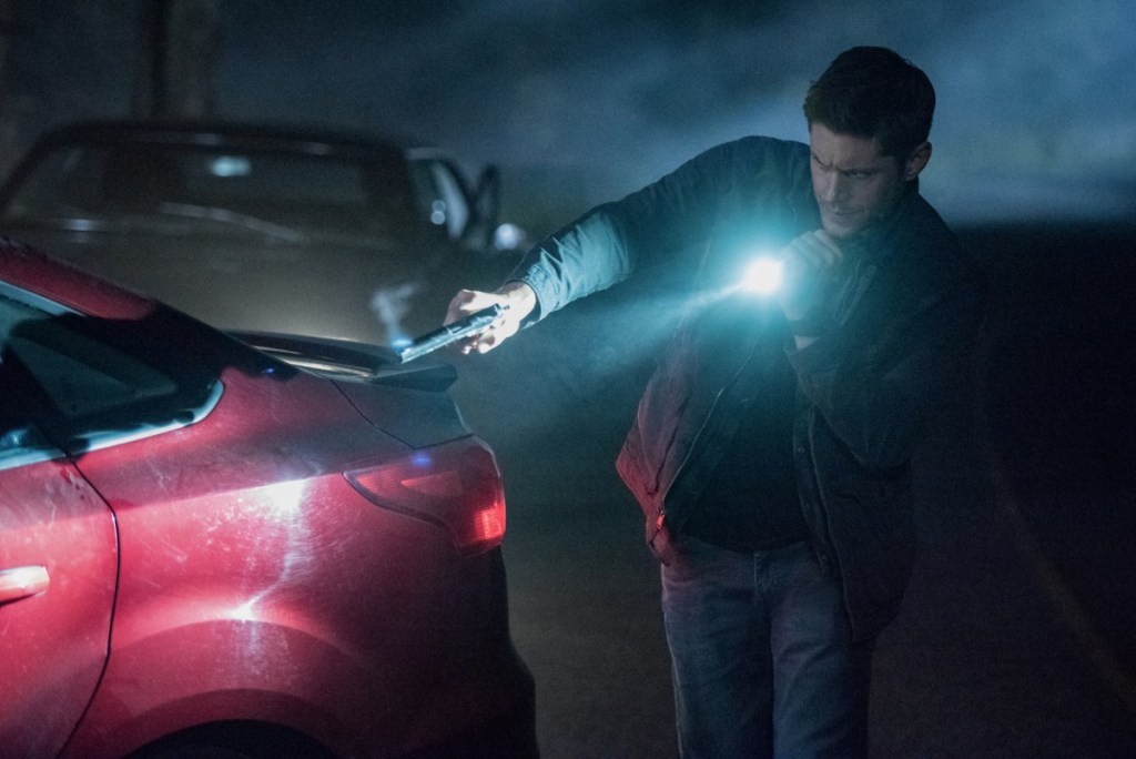 Dean (Jensen Ackles) arme et lampe torche en main, s'approchant d'une voiture